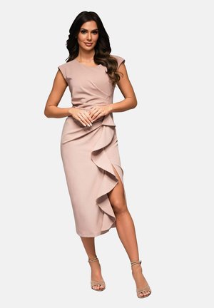 Robe nude ajustée avec manches courtes, détails en volants le long de la jupe et fente haute jusqu'à la cuisse. Portée avec des talons nus à lanières.
