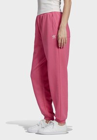 Pantalon de survêtement rose avec une taille élastique, des poches latérales et un petit logo Adidas blanc. Le tissu semble doux avec une coupe décontractée.