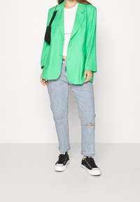 Vihreä ylisuuri bleiseri, valkoinen lyhyt toppi, vaaleansiniset kuluneet farkut ja mustat lenkkarit valkoisilla pohjilla. Bleiserissä on kaksi nappia ja taskut.