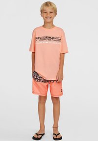 T-shirt rosa chiaro con grafiche logo in bianco e nero, abbinata a pantaloni corti rosa coordinati con un disegno nero e dettaglio logo laterale. Ciabatte.