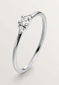 Anillo de plata con un diamante redondo central y dos diamantes más pequeños a cada lado. La banda es lisa y delgada, con un acabado pulido.