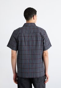 Camicetta a maniche corte con bottoni di colore navy con un motivo a scacchi rosso e beige. Tessuto morbido con una vestibilità rilassata e colletto a punta.