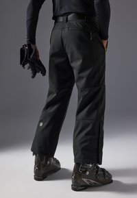 Pantalones de outdoor negros con un ajuste slim, que cuentan con bolsillos y detalles reflectantes, combinados con botas de esquí marrones. Tejido suave y costuras reforzadas.