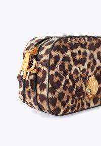 Tassel in panterprint, gemaakt van gestructureerde stof met een goudkleurige rits en hardware, met een decoratief embleem op de voorkant.
