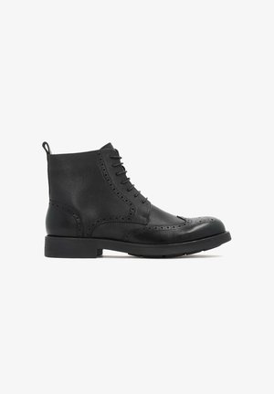 Bottine en cuir noir avec lacets à l'avant, détails de brogue, finition texturée et bout rond. Elle possède une semelle plate et une languette à l'arrière.