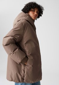 Giubbotto puffer marrone con cappuccio, caratterizzato da un esterno liscio e lucido, polsini a costine e tasche laterali. Vestibilità casual e rilassata.