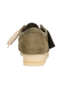 Mockagrön sko i mocka med en vit gummisula, rund tå och en distinkt tvinnad snöraccent bak.