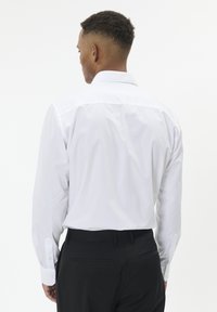 Valge pikade varrukatega särk tavalise krae ja nööpkäistega. Kandmine mustade pükstega, mis näitavad sujuvat ja poleeritud tekstuuri.