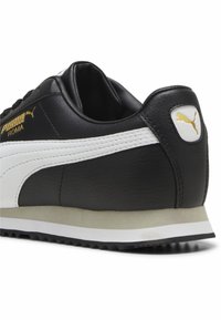 Baskets en cuir noir avec accents blancs, présentant une finition texturée, un col rembourré et un logo doré. Semelle extérieure en caoutchouc durable pour une bonne adhérence.