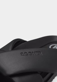 Gros plan sur des sandales noires à glissière avec des brides rembourrées embossées du logo "BOGNER" sur un fond clair uni.