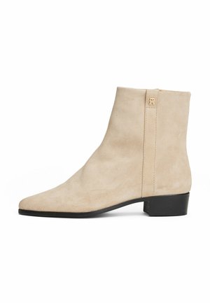 Stivaletto in suede beige con punta affusolata, design minimalista e tacco nero basso. Presenta una cerniera sul retro e un hardware con logo discreto.
