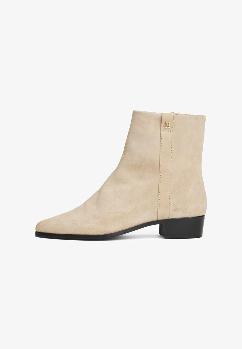 Bottines en daim beige avec un bout pointu, au design minimaliste et à petit talon noir. Comprend une fermeture éclair à l'arrière et un logo discret en métal.