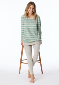 Lätt, grönrandig långärmad topp med rundad halsringning, kombinerad med beige leggings, båda i mjukt material. Modell sitter på en träpall.
