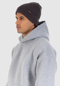 Beanie a coste di colore grigio scuro abbinato a una felpa con cappuccio grigia chiara caratterizzata da un piccolo logo sul petto e un fit comodo.