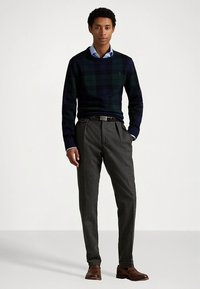 Marineblå og grønn rutete genser, lyseblå skjorte med krage, skreddersydde grå bukser og brune sko. Rene linjer og strukturert passform gjennom hele antrekket.