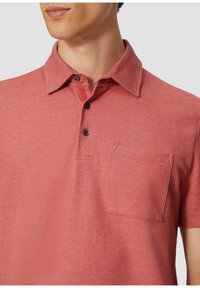 Kurzärmliges Poloshirt aus strukturiertem roten Stoff, mit einem Kragen, drei schwarzen Knöpfen und einer Brusttasche im rechteckigen Design.