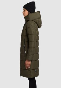 Lang olivengrøn puffcoat med hætte, lynlåslommer og quiltet mønster. Kombination med en sort strikket hue.