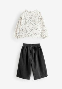 Vit långärmad skjorta med små bruna blommor, kombinerad med svarta kordshorts med elastisk midja och lös passform.