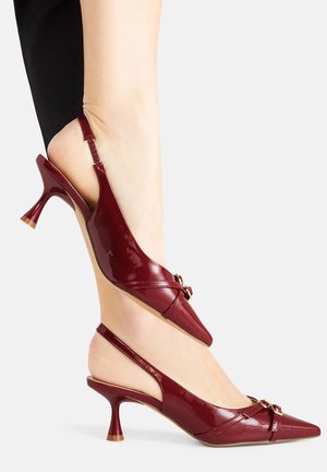 Burgundi színű lakkbőr slingback magassarkúk hegyes orral, alacsony, ívelt sarkú kivitelben, arany díszítéssel a lábfej részén. Simább felület.
