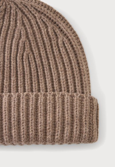 Bonnet en maille côtelée marron clair avec bord replié sur un fond clair uni.