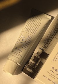 Rør med Dr. Althea 147 Barrier Cream i hvitt med strukturert hette, som har svart tekst og detaljert ingrediensliste. Accompanert av emballasje.