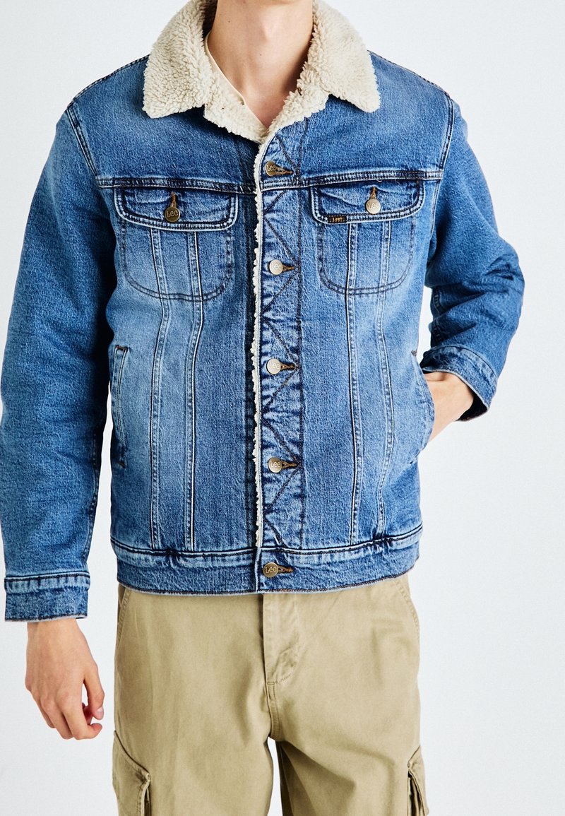 Jeansjacka med en ljusblå färg, en fluffig beige krage, två bröstfickor och framsida med knappstängning och märkestillbehör.