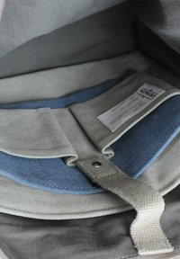 Grau gefüttertes Innere eines Rucksacks mit einem blauen Akzentpanel, grauer Tabverschluss und einem Pflegeetikett, das in das Futter eingenäht ist.