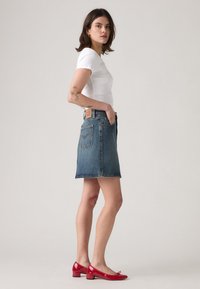 Top corto blanco ligero de manga corta combinado con una falda de mezclilla azul hasta la rodilla, con una etiqueta de cinturón de cuero marrón. Bailarinas de charol rojo.
