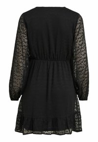 Svart klänning med en texturerad bodice, genomskinliga mönstrade ärmar, en åtsittande midja och en volangkant.