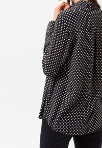 Svart skjorta med knappar som har vita prickar, med avslappnad passform, krage och långa ärmar. Tillverkad av lätt material med mjuk textur.