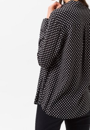 Black button-up shirt featuring white polka dots, with a relaxed fit, collar, and long sleeves. Made of lightweight fabric with smooth texture.