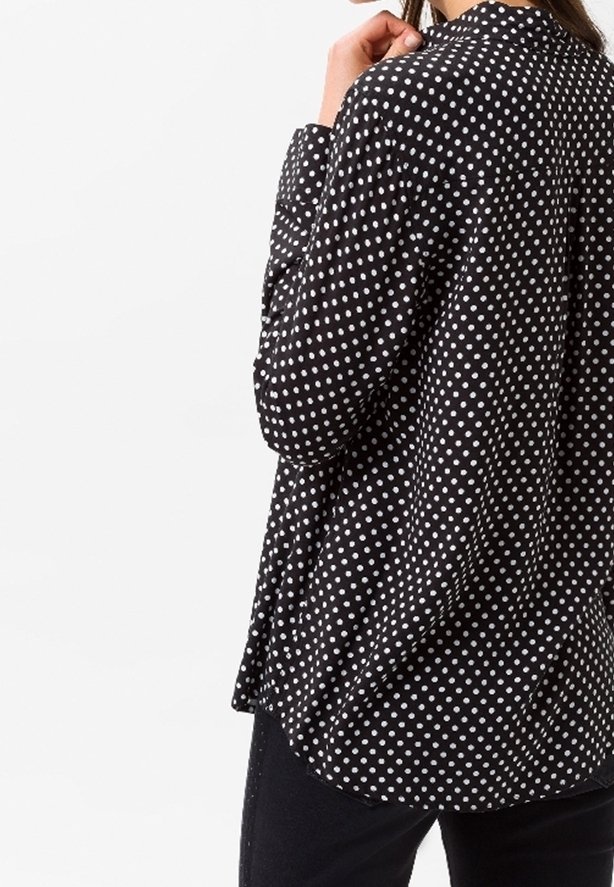 Svart skjorta med knappar som har vita prickar, med avslappnad passform, krage och långa ärmar. Tillverkad av lätt material med mjuk textur.