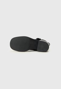 Semelle de chaussure noire en matériau en caoutchouc texturé et de forme effilée. Présente des boucles et une partie supérieure lisse qui se connecte à la semelle.