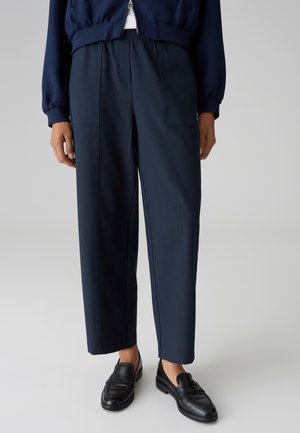 Marineblaue, hochtaillierte Hose mit elastischem Bund, ausgestattet mit zwei Vordertaschen und einem lockeren Schnitt, kombiniert mit schwarzen Slippers.