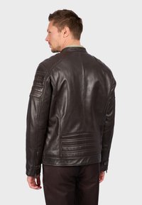 Hnědá kožená bunda s prošívanými rameny, zipovými detaily na manžetách a horizontálním prošíváním na zádech. Hladká textura.