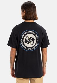 Camiseta de algodón negra con un gran diseño gráfico en la parte trasera, que incluye un logotipo circular con acentos azules y texto blanco.