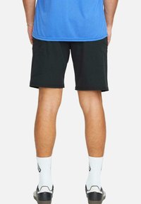 Pantalones cortos de carga negros mostrados desde atrás, con una textura suave, bolsillos laterales y detalles cosidos, combinados con calcetines blancos y zapatos negros.