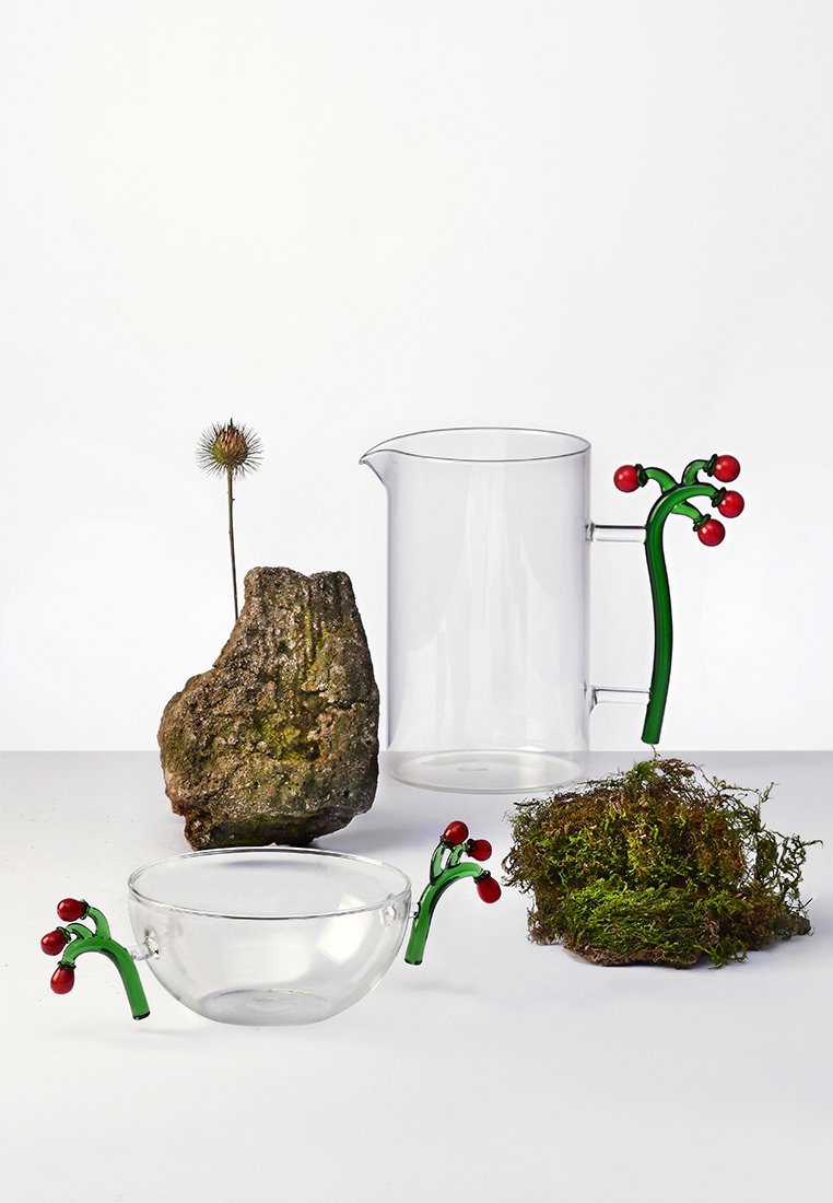 Przezroczysty dzbanek i miska z zielonymi uchwytami przypominającymi łodygi roślin oraz akcentami czerwonych jagód. Zawiera także kępkę mchu i kamień.