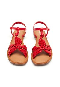 Sandales plates rouges avec des brides tressées, présentant un design tressé sur les orteils. Semelle intérieure beige et brides de cheville, accents matériels minimaux.