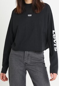 Czarna longsleeve z okrągłym dekoltem i białym logo "Levi's" na klatce piersiowej i na lewym rękawie. Zestawiona z ciemnoszarymi, wysokim stanem dżinsami.