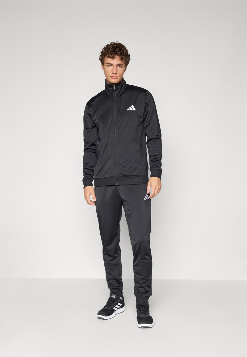 Black athletic tracksuit made of sleek fabric, featuring a zippered jacket and tapered pants, both adorned with the Adidas logo.