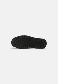 Black sneaker sole with a textured tread pattern, featuring raised sections and grooves for grip. Stamped brand logo visible.