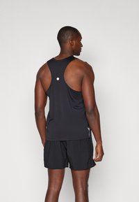 Sort atletisk tanktop med rygdesign i racerback, prydet med en hvid cirkulær detalje bagpå og parret med sorte shorts. Glat stof.