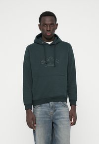 Hoodie vert en mélange de coton, avec une poche kangourou, un capuche avec cordon de serrage, et un logo "Originals" embossé sur la poitrine.