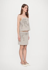 Set bestehend aus einem hellgrauen Tanktop und einem Rock mit floralem Reliefdesign. Weicher Stoff und taillierte Form, kombiniert mit weißen Mules.