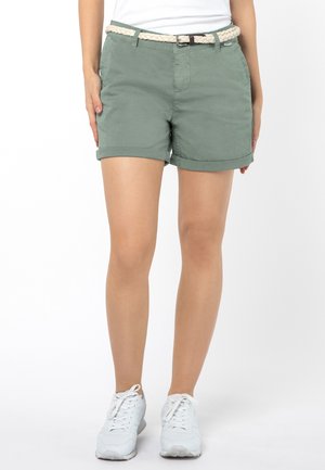 Groene katoenen shorts met een opgerolde zoom en een vlechtceintuur. Gecombineerd met witte sportieve schoenen. Eenvoudig ontwerp en een gladde textuur.