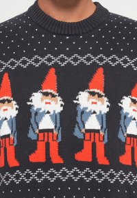 Dunkel gestrickter Pullover mit Gnommustern, roten Hüten und Stiefeln, blauen Mänteln, weißen Bärten und kleinen weißen Akzenten auf schwarzem Hintergrund.
