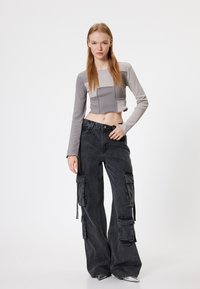 Top grigio a maniche lunghe tagliato con design a patchwork; abbinato a pantaloni cargo grigi scuri con grandi tasche e una vestibilità ampia.