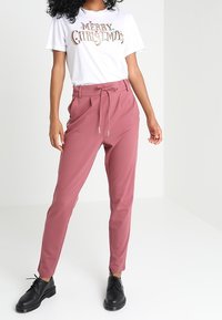 Lätta, rosa tapered byxor med dragsko i midjan, i kombination med en vit T-shirt med färgglad text. Svarta snörskor.