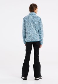 Fleecejacka i ljusblått med en texturerad, fluffig yta; hög krage; kombinerad med svarta, löst sittande byxor och robusta skor.